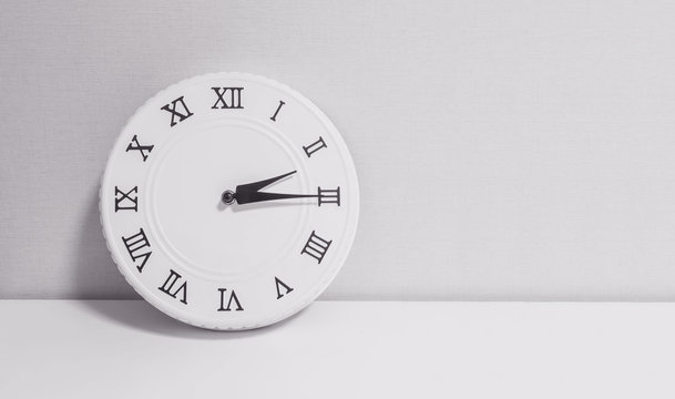 Closeup white clock for decorate show a quarter past two o'clock or 2:15 p.m. on white wood desk and wallpaper textured background in black and white tone with copy space