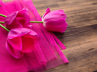 Pink tulips, floral arrangement on wooden background with pink mesh and space for message. Background for Mother's Day, 8 March and other greeting cards or invitations for lovely women. Soft focus.
