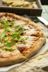 Italian pizza with cheese, tomatoes, olives and rucola on wooden table.