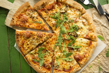 Italian pizza with cheese, tomatoes, olives and rucola on wooden table.