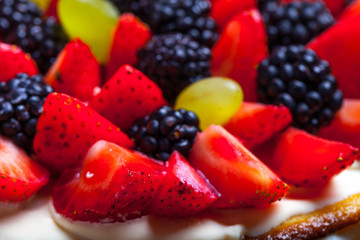 Top of biscuit homemade cake with cream and berries on black background. Selective focus. Shallow depth of field