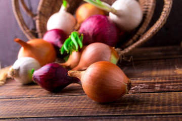 Different onions in basket on wooden background. Rustic style.  Red, white and golden.