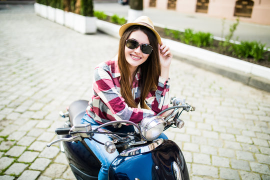 Close up lifestyle image of young fashionable woman in casual outfit sitting on scooter on the street. Tourist woman enjoying holidays .