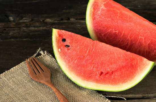 the watermelon on a rustic wooden table background with wood fork and sack cloth