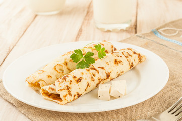 Food photography. Thin pancakes with filling and slices of cheese with herbs