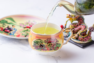 A cup of green tea on a white background. Hot drink pours into a cup with a pattern.