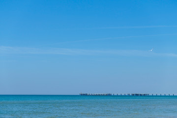 Naklejka na ściany i meble Pier in the black sea in the distance on the background of blue clear Sunny sky