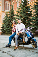 Fashionable couple posing on the street, siting on scooter , wearing stylish casual clothes.