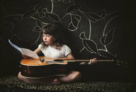 Little girl with a guitar and musical notes sitting on the couch.