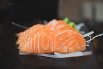 Salmon raw sashimi on black Japanese traditional dish on black table. Closed up.