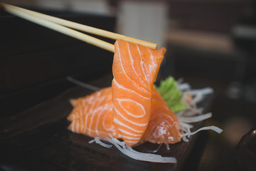 Salmon raw sashimi on black Japanese traditional dish on black table. Closed up.