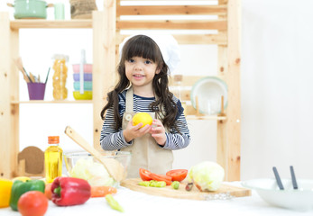 Beautiful kid girl cooking and cutting vegetables on kitchen