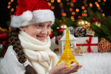 child girl portrait with eiffel tower and christmas decoration, dark background with lights, face expression and happy emotions, dressed in santa hat, winter holiday concept