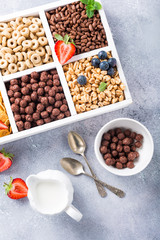 Milk jug and variety of cold quick breakfast cereals with berries in white wooden box, healthy eating concept, top view.