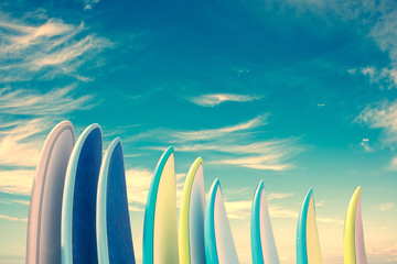 Stack of colorful surfboards on blue sky background with copy space, retro vintage filter