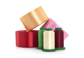 Threads on reels and satin ribbons for needlework on a white background