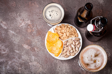 Beer in bottles and glasses on the concrete table. Beer and snacks are pistachio nuts, chips and nachos top view. Copy space. Drink and snack for the football match or rest in pub