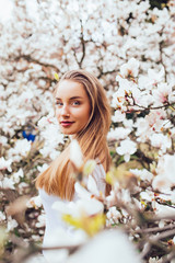 beautiful young blond woman surrounded with magnolia flowers in spring garden