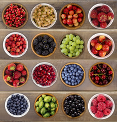 Collage of different fruits and berries on a wooden background. Collection of fruits and berries in a bowl. Top view.