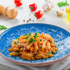 Tasty Italian penne pasta with tomato sauce on a blue rustic plate. Delicious healthy Italian food on a white wooden table.