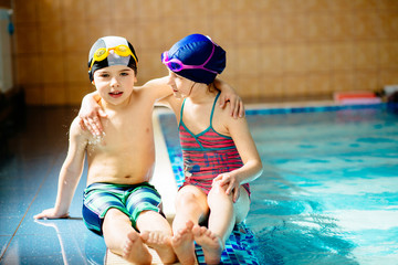 Happy children sitting on edge of the swim pool. Sport, recreation and childhood concept.