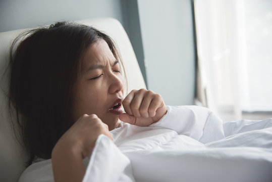 Asian woman having a cold. Girl is coughing on her bed. Illness, disease concept.