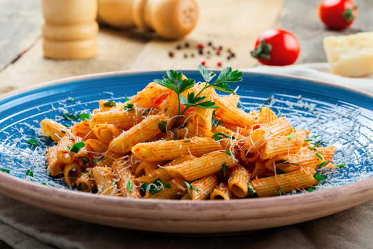 Italian penne pasta with arrabiata tomato sauce and parsley on a blue rustic plate. Traditional Italian healthy cuisine. Close-up shot.