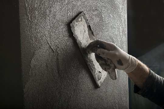 Hand of a construction worker plastering and smoothing concrete wall close-up.