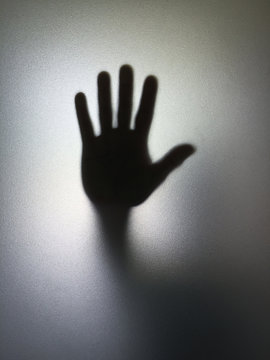 Man or woman showing stop gesture hand silhouette through frosted glass