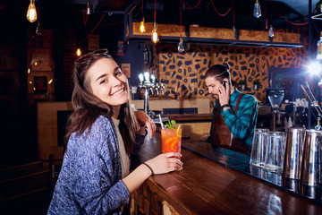 A girl with  cocktail smiles behind counter at the bar.