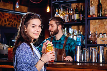 A girl with  cocktail smiles behind counter at the bar.