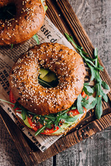 Bagels with cream, avocado, tomatos and arugula on wooden board and table background. Healthy...