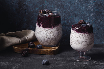 Organic chia pudding in two glasses with coconut milk and blackberry smoothie on top. Dark rustic...