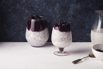 Organic chia pudding in two glasses with coconut milk and blackberry smoothie on top. Dark rustic...