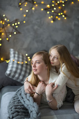 Blonde mom and teen daughter hug on bed