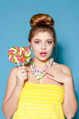 Portrait of a beautiful young woman with candy on a blue background. The blonde with the colored candy. Sweet. Woman with bright