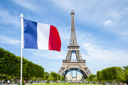 French flag flying in bright blue sky above the Eiffel Tower in Paris, France