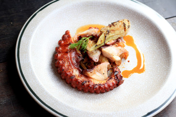 Grilled octopus tentacles with lemon and parsley leaves on dish.