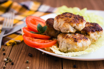 Готовые мясные котлеты с помидорами на тарелке