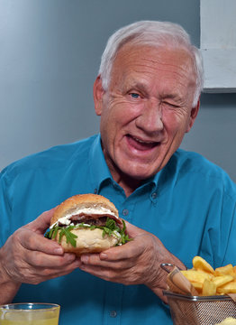 Anciano gracioso comiendo hamburguesa.