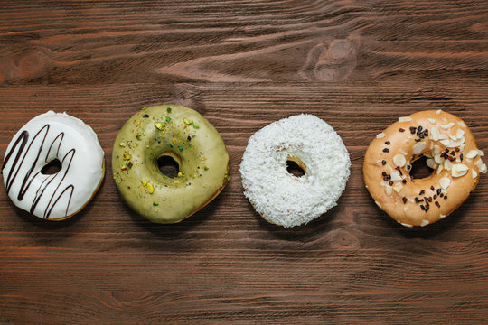 Four glazed donuts placed in line on dark background. Almond, coconut, caramel, white chocolate donut.