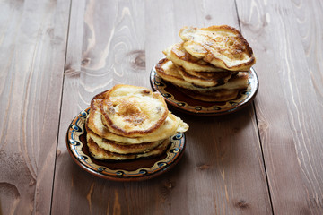 pancakes to a painted clay saucer on wooden background