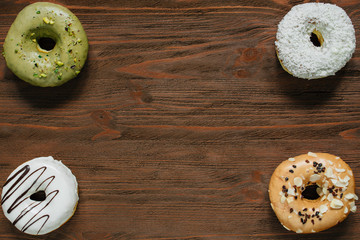Four glazed donuts placed in corners on dark background. Almond, coconut, caramel, white chocolate donut.
