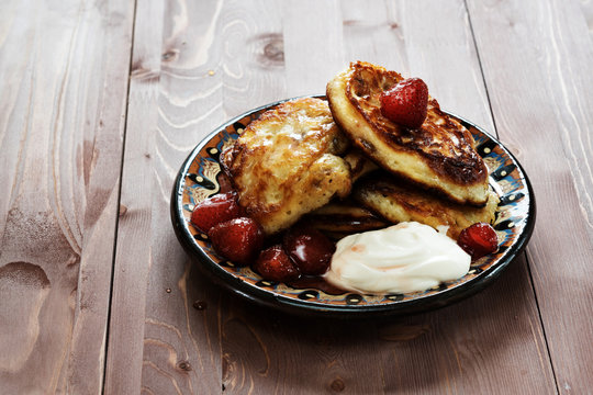 pancakes with sour cream and strawberry jam on a clay plate