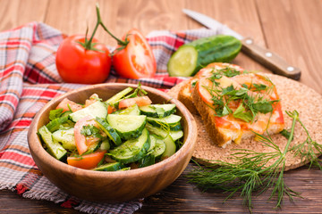 Салат из огурцов и помидоров в деревянной тарелке, запеченные бутерброды с сыром и овощи на столе