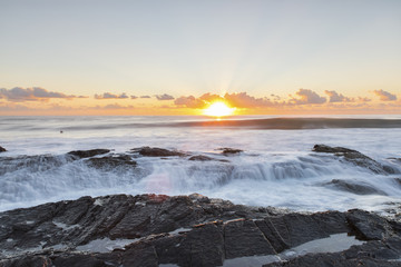 Ocean sunrise with ocean cascading over the end of Currumbin Rock. Gold Coast.