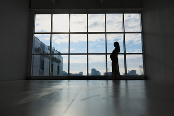 Fototapeta na wymiar Pregnant woman stands by the window