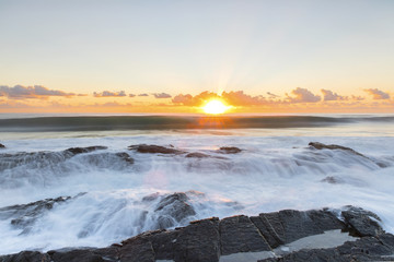 Ocean sunrise with ocean cascading over the end of Currumbin Rock. Gold Coast.