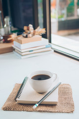 Cup of hot coffee and brown note book on table.