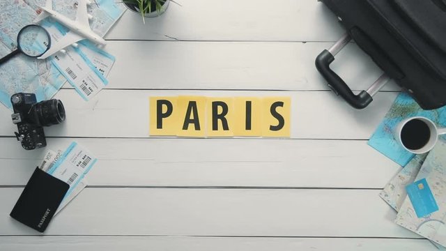 Top view time lapse hands laying on white desk word "PARIS" decorated with travel items